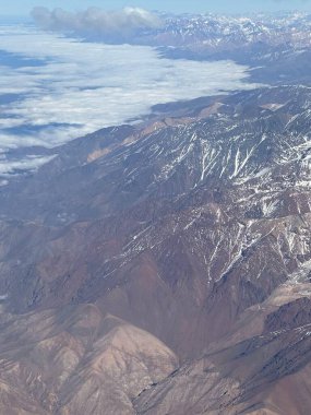 Karla kaplı dağların etkileyici hava manzarası yoğun bulutlar ve derin vadilerle çelişiyor. Görkemli sahne, kumral ve gri engin toprak tonlarını ortaya çıkarıyor. Kardan gelen beyaz dokunuşlarla..