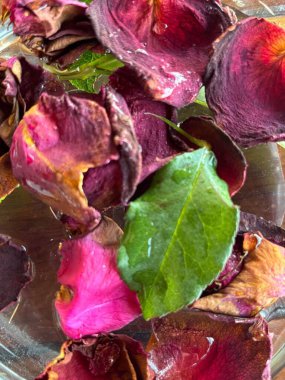 Parlak yeşil yapraklarla karıştırılmış kırmızı, pembe ve mor tonlardaki gül yapraklarının güzel bir kompozisyonu doğal bir zarafet ve dinginlik yaratıyor. Su canlı renkleri yansıtır, düzenlemeye ferahlatıcı bir dokunuş ekler..