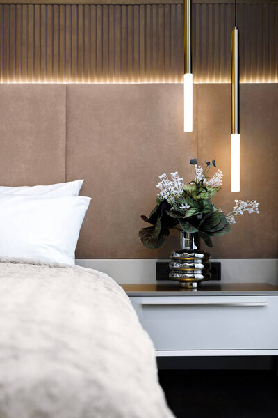 Современная спальня с уютной кроватью, современным освещением и элегантной цветочной композиции. Высокое качество фото