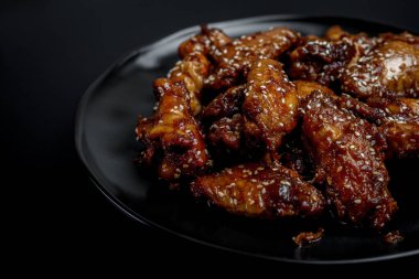 Yapışkan soya sosuna bulanmış tütsülenmiş tavuk kanatları siyah bir tabakta servis ediliyor ve arka planda dumanlar yükseliyor. Yüksek kalite fotoğraf