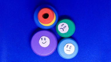 Renkli ahşap oyuncaklar, farklı duygular ifade eden, canlı mavi bir arkaplan üzerine kurulmuş..