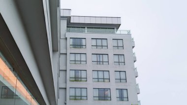 Camdan balkonları ve pencereleri olan modern otel cephesi, alçak bir açıdan görülüyor..