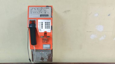Yıpranmış bir duvara monte edilmiş turuncu bir ankesörlü telefon. Nostalji ve iletişim konsepti.