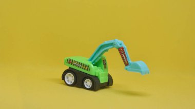 Sarı arka planda yeşil oyuncak kazıcısı. İnşaat, inşaat veya çocukluk temalı projeler için ideal.