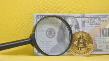 Bitcoin 'in yakın plan çekimi ve bir büyüteç altında Amerikan Doları destesi. Kripto para birimi kavramı geleneksel para birimine, finansal analize ve yatırıma karşı.