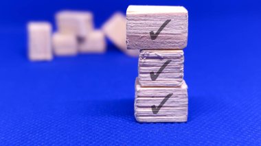 Mavi arka planda kontrol işaretleri olan üç tahta blok. Konseptler: görev tamamlama, onay, başarı.