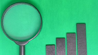 Yeşil zemin üzerinde yükselen siyah çubukların yanında büyüteç, büyüme analizi ve iş ilerlemesini simgeliyor.