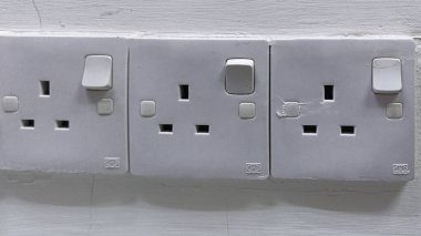 Beyaz bir duvarda üç İngiliz prizi ve düğmesi var. Ev elektriği ve güç kaynağı.