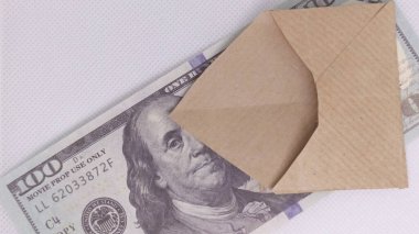 Düz kahverengi bir zarf sahte bir dolar banknotunu gizler, gizli ödemeleri, rüşveti veya yasadışı faaliyetleri ima eder.