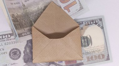 Birkaç yüz dolarlık banknotların üzerinde açık duran basit kahverengi bir zarfın üstünden bir kare..