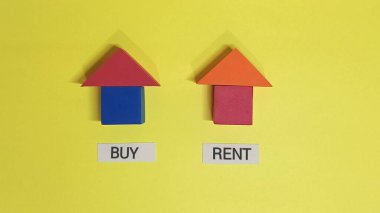 Renkli bloklardan yapılmış iki küçük ev, pek çok insanın karşı karşıya olduğu ortak mali tercihi gösteren parlak sarı bir arka plana karşı bir ev satın alma veya kiralama kararını temsil ediyor.