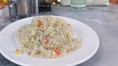 Kızarmış tavuklu pilav yenmeye hazır olarak beyaz bir tabakta oturur. Pirinç taneleriyle karıştırılmış havuç ve yumurta parçalarıyla lezzetli ve tatmin edici bir yemek sunar.