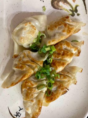 Süslü bir tabakta taze doğranmış frenk soğanıyla servis edilen bir tabak kızarmış altın gyozas. Sunum iştah açıcı, zevki ve tatmini çağrıştırıyor..