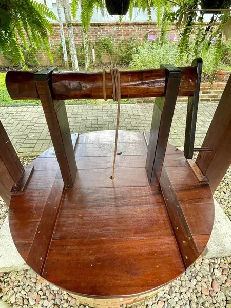 Sağlam bir yapısı ve karanlık ahşap detayları olan eski bir ahşap pres, açık havada duruyor. Yeşil yeşillik arka planı, gelenekleri yakalamak ve tarih yazmak için mükemmel bir köy ve dingin bir alan olduğunu gösteriyor..