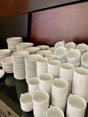 Beyaz tabak ve fincanlardan oluşan geniş bir düzenleme düzgün dizilmiş, basit şekiller ve zarif çizgiler sergiliyor. Resim bir organizasyon ve minimalizm duygusu taşır, yemek ayarları veya etkinlikler için idealdir.