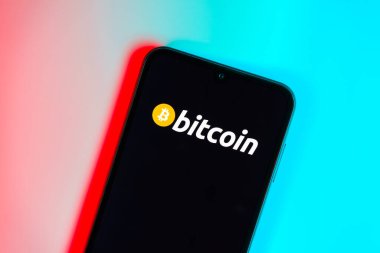 Prag, Çek: Mavi yüzey arka planında bitcoin logosuna sahip modern akıllı telefon aygıtı.