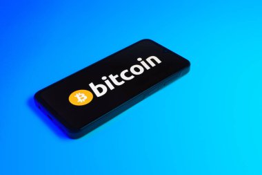 Prag, Çek: Mavi yüzey arka planında bitcoin logosuna sahip modern akıllı telefon aygıtı.