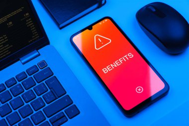 Ofis masasında bilgisayar faresi ve dizüstü bilgisayarlı akıllı telefon ekranda metni gösteriyor