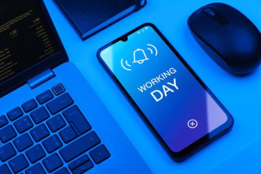 Ofis masasında bilgisayar faresi ve dizüstü bilgisayarlı akıllı telefon ekranda metni gösteriyor