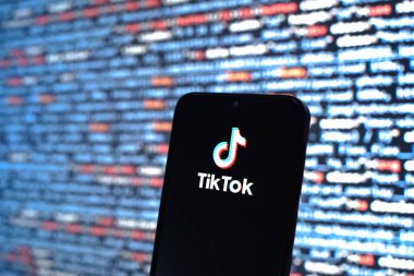 Prag, Çek Cumhuriyeti - 05: 18 2025: Kaynak kod arkaplanı önündeki bir akıllı telefon TikTok logosunu görüntüler.