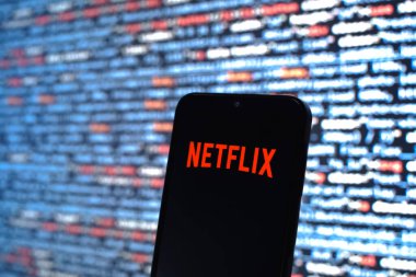 Prag, Çek Cumhuriyeti - 05: 18 2025: Kaynak kod arkaplanı önündeki bir akıllı telefon Netflix logosunu görüntüler.