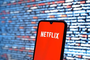 Prag, Çek Cumhuriyeti - 05: 18 2025: Kaynak kod arkaplanı önündeki bir akıllı telefon Netflix logosunu görüntüler.