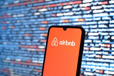 Prag, Çek Cumhuriyeti - 05: 18 2025: Kaynak kod arkaplanı önündeki bir akıllı telefon Airbnb logosunu görüntüler.