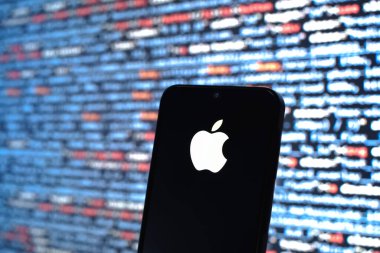 Prag, Çek Cumhuriyeti - 05: 18 2025: Kaynak kod arkaplanı önündeki bir akıllı telefon Apple logosunu görüntüler.