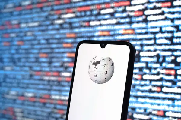 Prag, Çek Cumhuriyeti - 05: 18 2025: Kaynak kod arkaplanı önündeki bir akıllı telefon Wikipedia logosunu görüntüler.