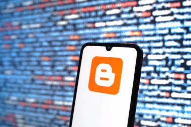Prag, Çek Cumhuriyeti - 05: 18 2025: Kaynak kod arkaplanı önündeki bir akıllı telefon Blogger logosunu görüntüler.