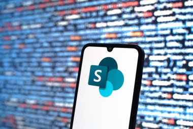Prag, Çek Cumhuriyeti - 05: 18 2025: Kaynak kod arkaplanı önündeki bir akıllı telefon Microsoft Sharepoint logosunu görüntüler.