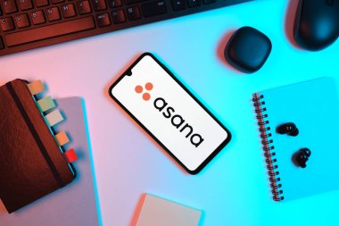 Prag, Çek Cumhuriyeti - 05: 18 2025: Asana logosunu gösteren bir telefonla ofis masasına yerleştirilmiş nesneler.