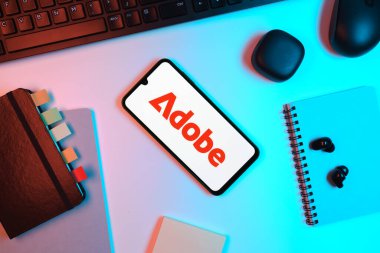 Prag, Çek Cumhuriyeti - 05: 18 2025: Adobe logosunu gösteren bir telefonla ofis masasına yerleştirilmiş nesneler.