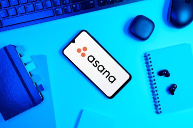 Prag, Çek Cumhuriyeti - 05: 18 2025: Asana logosunu gösteren bir telefonla ofis masasına yerleştirilmiş nesneler.