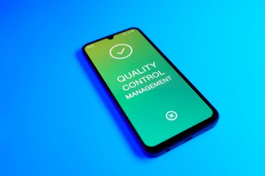 Açık mavi arkaplandaki telefon Kalite Kontrol Yönetimi metnini görüntüler.