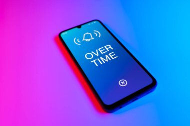 Mor ve mavi arkaplan üzerindeki telefon Fazla mesai metnini görüntüler.