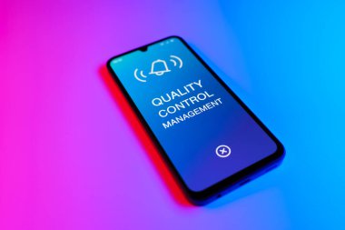 Mor ve mavi arkaplandaki telefon Kalite Kontrol Yönetimi metnini görüntüler.