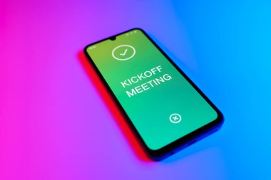 Mor ve mavi arkaplan üzerindeki telefon Kickoff Toplantı metnini görüntüler.