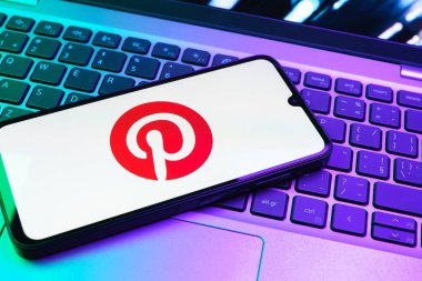 Prag, Çek Cumhuriyeti - 08 01 2025: Dizüstü bilgisayarın üzerinde duran bir cep telefonu Pinterest logosunu gösteriyor. Pinterest fikirleri görsel olarak keşfetmek ve kaydetmek için bir platformdur..
