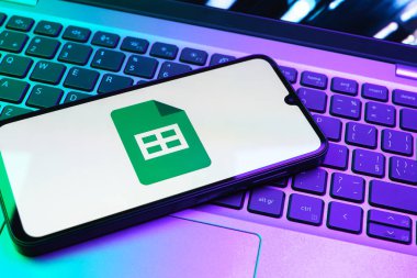Prag, Çek Cumhuriyeti - 08 01 2025: Laptop klavyesinde duran bir cep telefonu Google Sheets logosunu görüntüler. Google Sayfalar tablo oluşturmak ve yönetmek için bir platformdur.