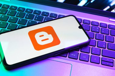 Prag, Çek Cumhuriyeti - 08 01 2025: Dizüstü bilgisayarın üzerinde duran bir cep telefonu Blogger logosunu gösterir. Blogger blog oluşturma ve yayınlama için bir platformdur.