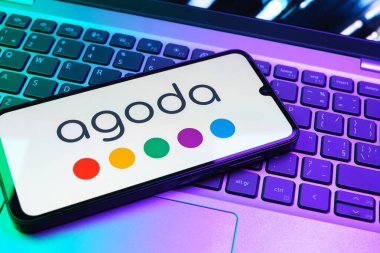 Prag, Çek Cumhuriyeti - 08 01 2025: Dizüstü bilgisayarın üzerinde duran bir cep telefonu Agoda logosunu gösteriyor. Agoda, otelleri ve seyahat yerlerini ayırtmak için bir platform..