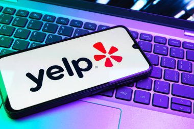 Prag, Çek Cumhuriyeti - 08 01 2025: Laptop klavyesinde duran bir cep telefonu Yelp logosunu gösterir. Yelp yerel işletmeleri bulmak ve incelemek için bir platformdur.