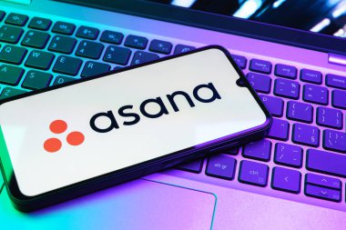 Prag, Çek Cumhuriyeti - 08 01 2025: Dizüstü bilgisayarın üzerinde duran bir cep telefonu Asana logosunu gösterir. Asana görev yönetimi ve takım işbirliği için bir platformdur..
