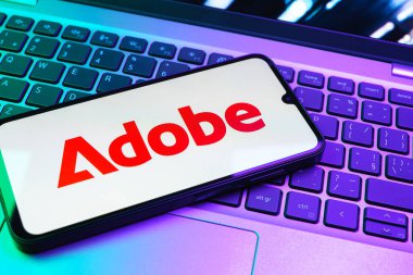 Prag, Çek Cumhuriyeti - 08 01 2025: Dizüstü bilgisayarın üzerinde duran bir cep telefonu Adobe logosunu gösterir. Adobe yaratıcı araçlar ve hizmetler sunan bir yazılım şirketidir..