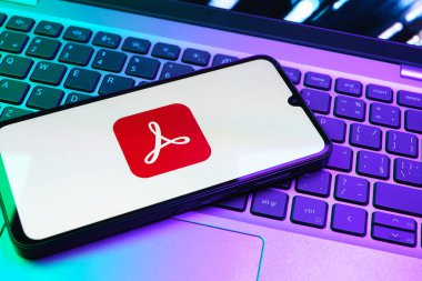 Prag, Çek Cumhuriyeti - 08 01 2025: Dizüstü bilgisayarın üzerinde duran bir cep telefonu Acrobat Reader logosunu gösteriyor. Acrobat Reader, PDF belgelerini görüntülemek ve yönetmek için bir platformdur.