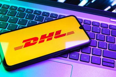 Prag, Çek Cumhuriyeti - 08 01 2025: Dizüstü bilgisayarın üzerinde duran bir cep telefonu DHL logosunu gösterir. DHL uluslararası nakliye hizmeti sunan bir lojistik şirketidir..