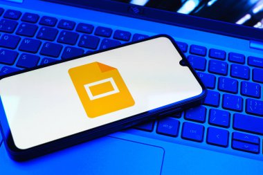 Prag, Çek Cumhuriyeti - 08 01 2025: Laptop klavyesinde duran bir cep telefonu Google Slides logosunu görüntüler. Google Slides sunumlar ve slayt gösterileri oluşturmak için bir platformdur.
