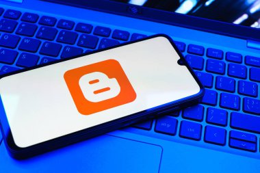Prag, Çek Cumhuriyeti - 08 01 2025: Dizüstü bilgisayarın üzerinde duran bir cep telefonu Blogger logosunu gösterir. Blogger blog oluşturma ve yayınlama için bir platformdur.