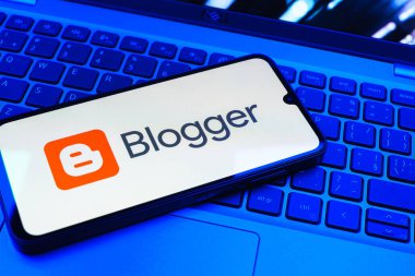Prag, Çek Cumhuriyeti - 08 01 2025: Dizüstü bilgisayarın üzerinde duran bir cep telefonu Blogger logosunu gösterir. Blogger blog oluşturma ve yayınlama için bir platformdur.